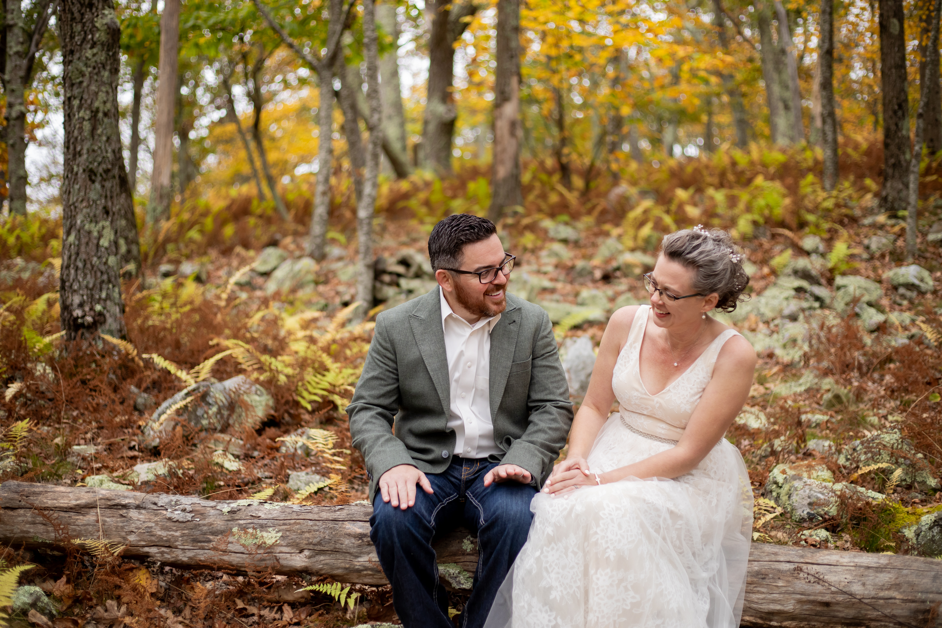 Couple laughing together on a fallen log surrounded by fall ferns and foliage in Shenandoah National Park