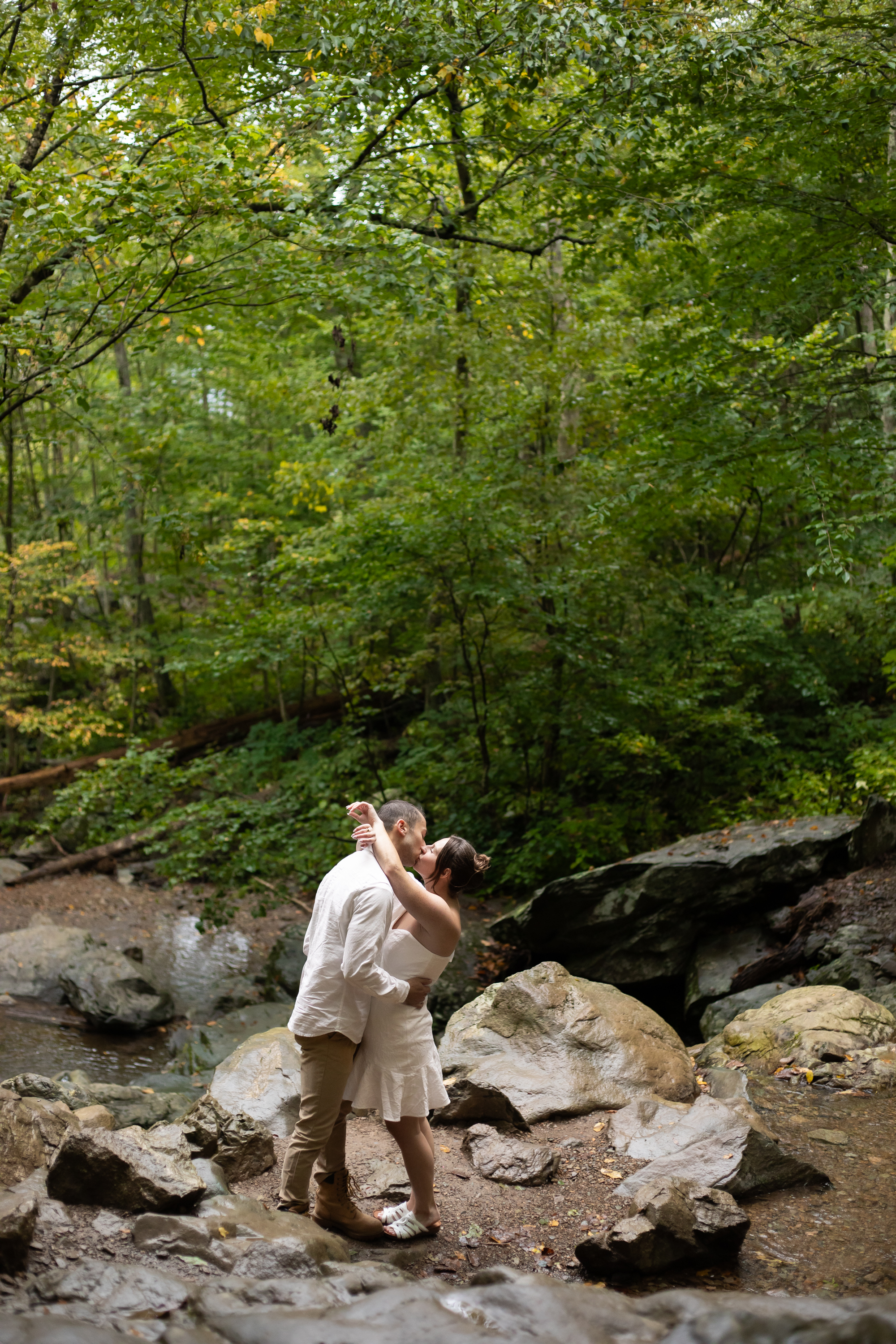 Couple kissing among rocks and lush summer forest at Dark Hollow Falls