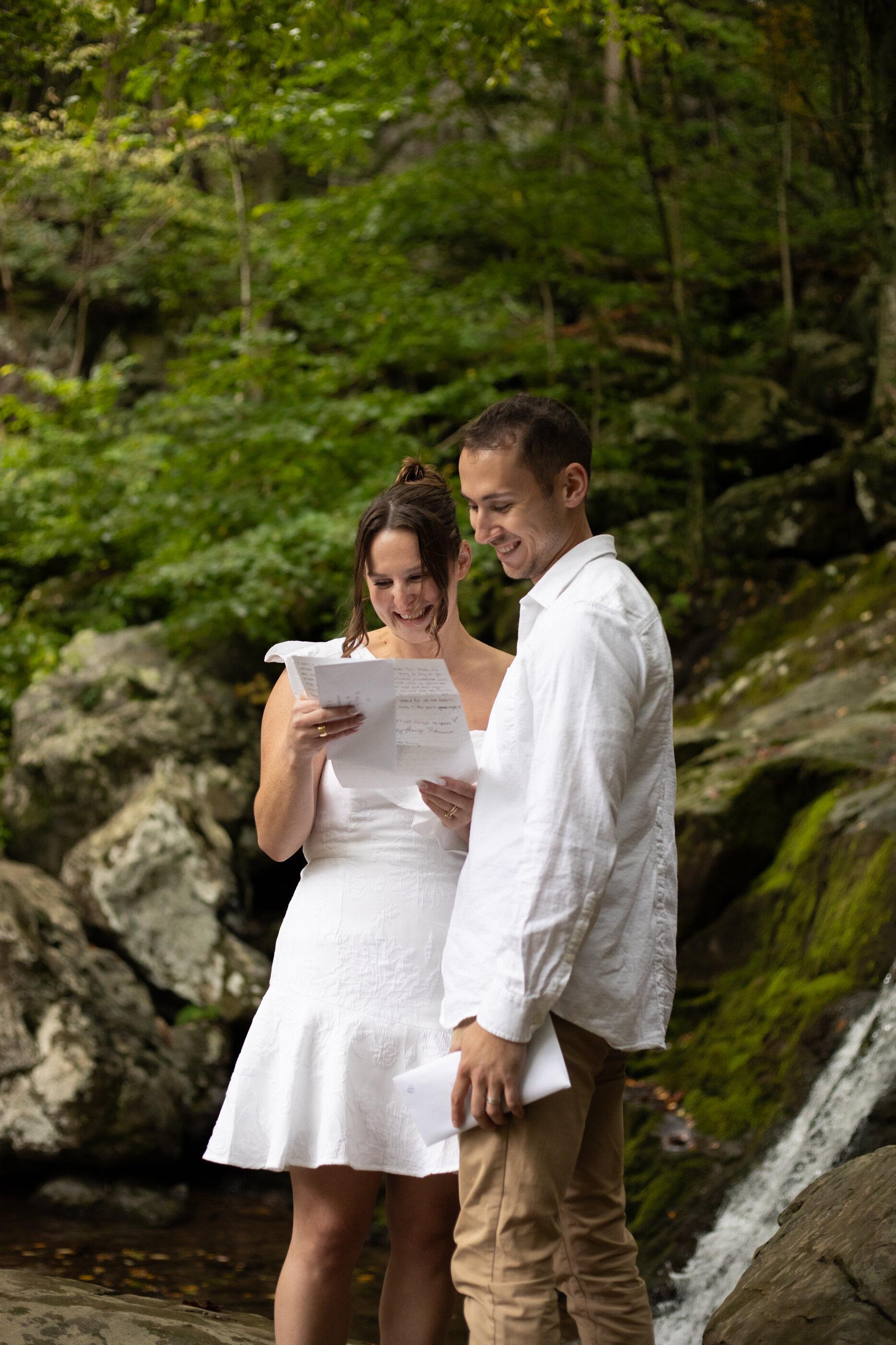 Couple reading vows together at a waterfall in a lush green Virginia forest