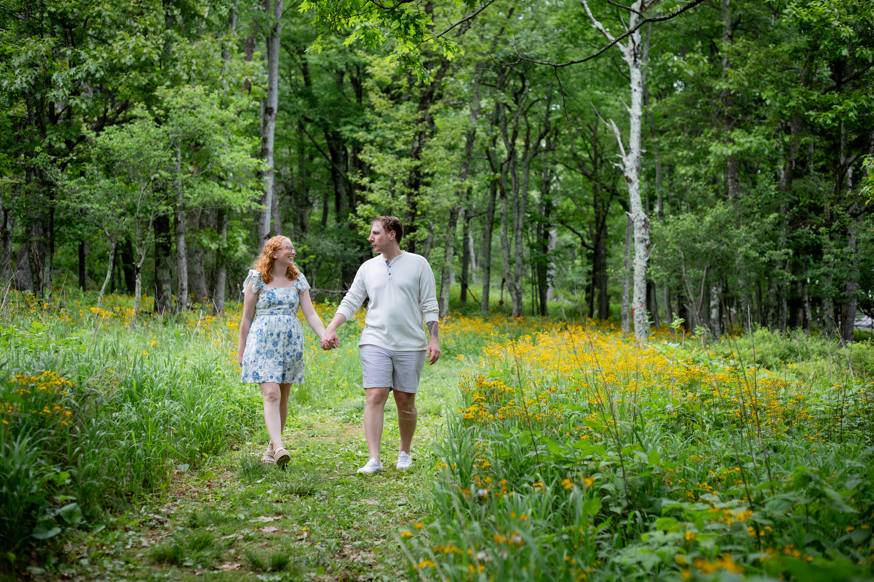 Couple walking hand in hand through a lush green forest path lined with yellow wildflowers in Shenandoah National Park in spring