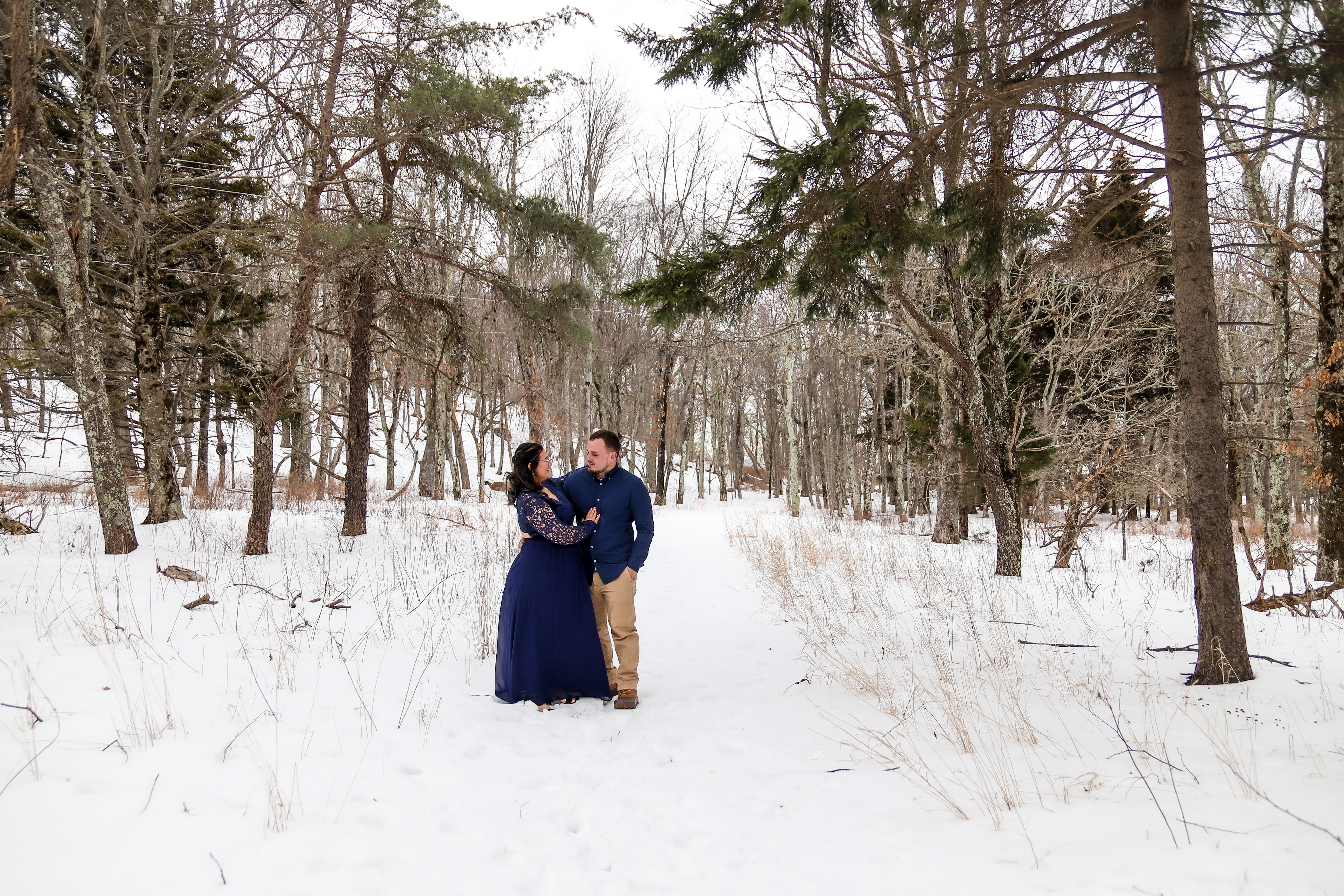 Couple in navy blue embracing on a snow-covered forest path at Big Meadows in Shenandoah National Park